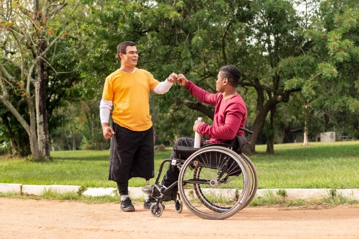 A disabled man sitting in his wheelchair and another disabled man doing fist bump