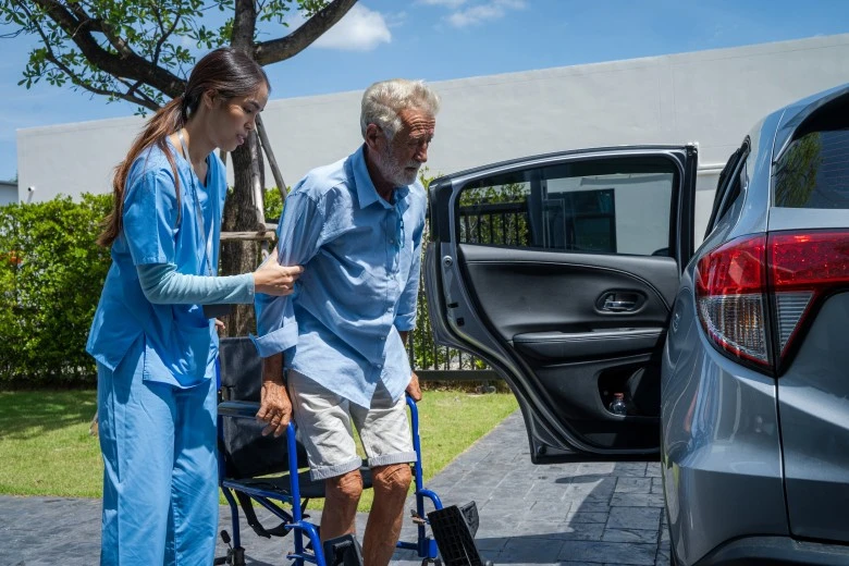 A disabled man sitting in his wheelchair and his support worker assisting him in to the car